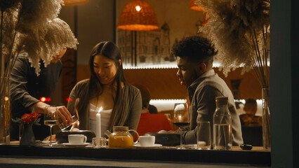 African american man and asian woman sit in modern gastro cafe together. The chef serves delicious...