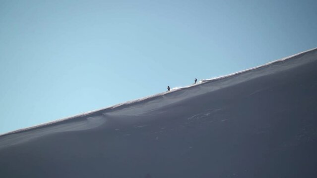 Two skiers and snowboards silhouette at distance atop mountain cornice making turns down deep fresh powder snow at Vail Pass Colorado