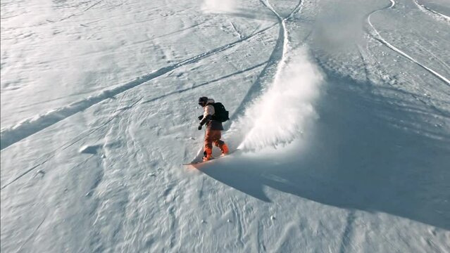 FPV Male Snowboarder riding down fresh powder snow followed blue sky steep turns sunset at Vail Pass Colorado