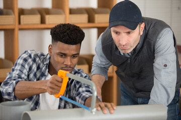 supervisor watching apprentice plumber modify a pipe with a saw