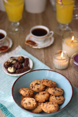 Plate of chocolate pralines, bowl of cookies, cups of tea, glasses of juice and lit candles on the table. Selective focus.