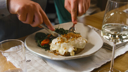 Close up shot of guest cutting meat dish and tasting gourmet food in gastro cafe. Plate with fresh salad and beef under cheese. Dinner in restaurant with modern cuisine. Public eating concept.