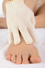 Young healthy woman massages the back of her foot with a massage glove during relaxation, wellness...