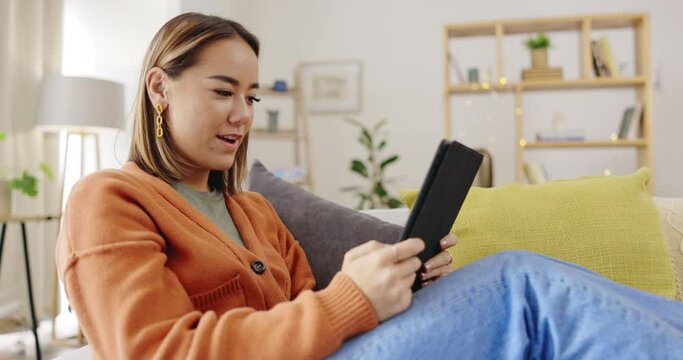 Video call, sofa and woman on tablet waves hello for virtual communication, talking and social networking. Home, happy and asian person relax on couch with digital technology and online web chat