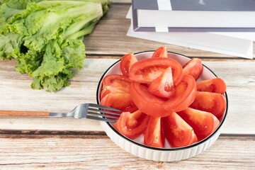 Closeup of delicious slices of juicy red tomatoes in a round bowl with a fork resting against it