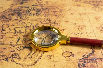 Closeup of a vintage magnifying glass with a gold frame laying on an old brown treasure map