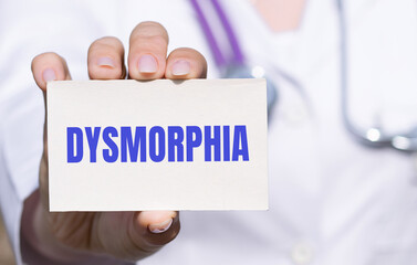 Dysmorphia - word on card in doctors hand, body dysmorphic disorder concept, gray background