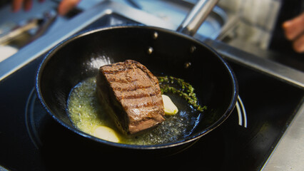 The chef cooks delicious meal on stove. The cook fries piece of juicy pork meat on frying pan with...