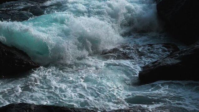 Slow motion. Top view. Brightly turquoise waves break into white foam on the coastal cliffs and seethe between them. Tourist attraction. Itinerary for hiking on a weekend or holiday. Leisure.