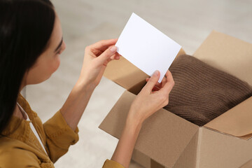 Woman holding greeting card near parcel with Christmas gift indoors, closeup