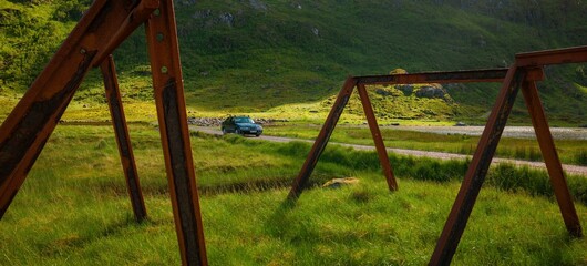 Fototapeta premium Lone car travelling on a rode at a rural landcape in Lofoten, Norway