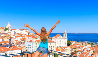 Woman with arms raised holding portuguese flag looking at viewpoint of Lisbon