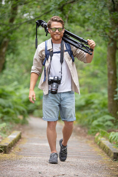 male photographer walks with tripod on his shoulder