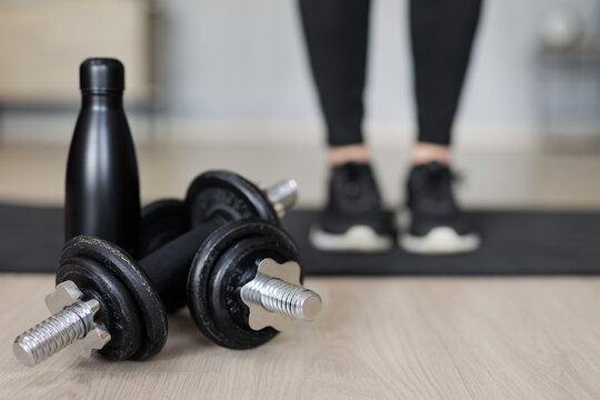 sport and fitness background - close up of black dumbbells and bottle of water, female legs on yoga mat