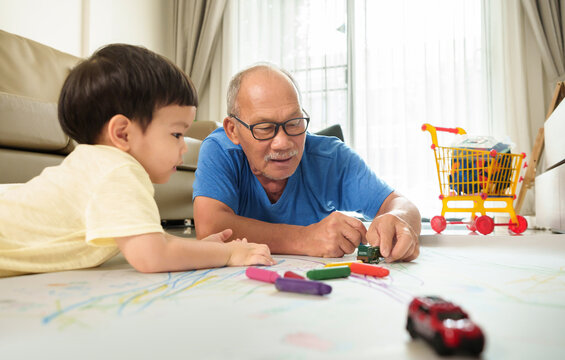 Happy Asian Senior Japapnese man and little child boy lying on floor playing together. Grandfather and Grandson enjoying painting with colorful Crayons on paper.