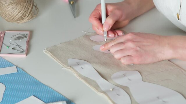 Animation of cropped woman hands drawing and contouring paper sewing patterns on textile fabric on white table. Needlework patterns, entrepreneur, tailor working in atelier, workshop. Video, 4k