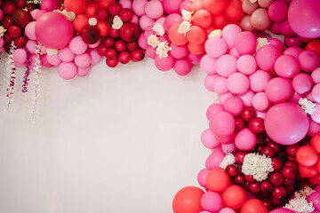 Trendy spring decor. Arch with balloons, flowers for party. White photo wall decoration space or place with pink, red, maroon, burgundy balloons. Celebration concept. Birthday party. Wedding reception