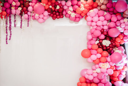 Arch with balloons, party decor. White photo wall decoration space or place with pink, red, maroon, and burgundy balloons. Trendy spring decor. Celebration concept. Birthday party. Wedding reception.