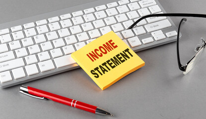 INCOME STATEMENT text on a sticky with keyboard, pen glasses on grey background