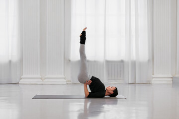 Professional instructor young woman does sarvangasana during a yoga class in a white light studio....