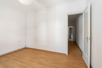 An empty small bright room with white walls and an open door overlooking a corridor in a spacious house. The concept of a room in a hotel or moving. Copyspace