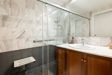 Comfortable modern bathroom with a glass-walled shower, sink with wooden cabinet and mirror in a new apartment. The concept of a stylish but concise design