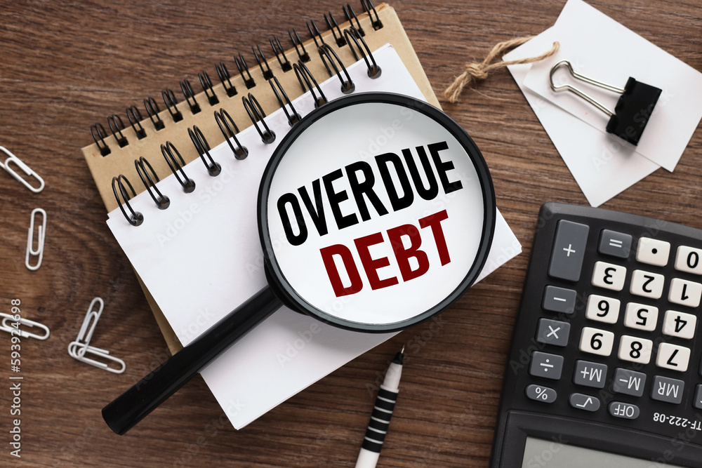Poster overdue debt wooden background with text on magnifier glass. two notepads and a calculator