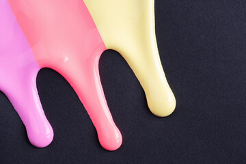 Rainbow liquid drops of paint color flow down on black paper. Abstract art. Multicolored paint dripping on the black wall