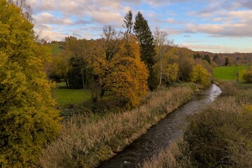 Fototapeta na wymiar Small creek flowing through idyllic landscape during late autumn