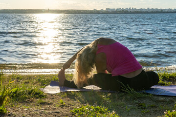 A woman in sports clothes, sitting in the lotus position and bending her hand to her leg on a rug...