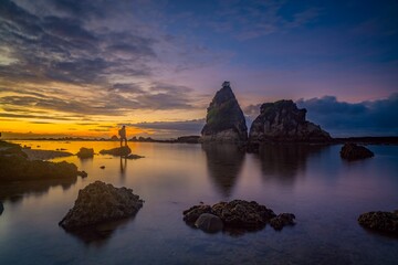 Person on unique rock formations on sandy Tanjung Layar Beach under dark cloudy sunset sky - Powered by Adobe