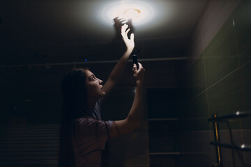 Woman young holding hand flashlight in darkness. Disconnecting home electricity and changing lamp bulb