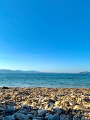 Fototapeta na wymiar Beach in Greece, mountains in the background. A striking contrast of white walls and green trees, many shades of blue and earth tones under a hazy sky. Walk in nature. 