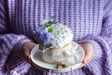 A woman holds in her hands an Easter cake with meringue and decor in a plate
