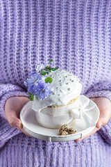 A woman holds in her hands an Easter cake with meringue and decor in a plate