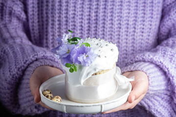 A woman holds in her hands an Easter cake with meringue and decor in a plate
