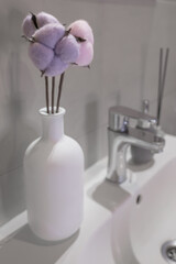 Three cotton flowers in a white vase in the bathroom. Naturalness in the interior. Natural...