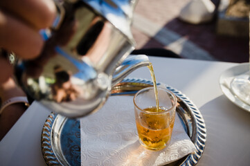 Fototapeta na wymiar Pouring traditional Moroccan tea pot with a cup outside ready to drink