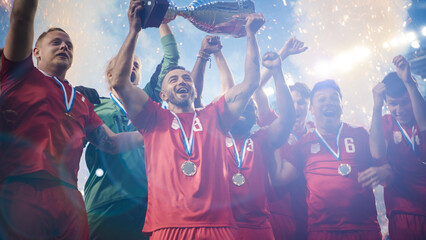 Fototapeta na wymiar Football Finals Tournament Winning Team Celebrates Victory Cheering and Lifting Trophy Prize, Showing it to the Whole Stadium Arena. Happy Soccer Players, Champions of International Championship Cup