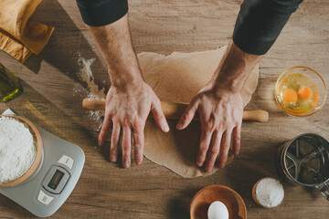 Unrecognizable man rolling out the dough with a rolling pin on wooden background