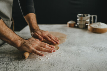 Unrecognizable man rolling out the dough with a rolling pin on black background