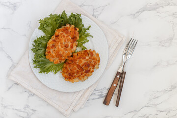 Pozharsky cutlets and lettuce leaf in a white plate on a marble background. Selective focus, top view, place for text