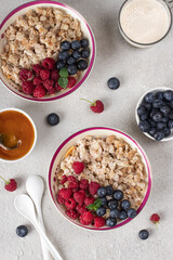 Oatmeal porridge with blueberries, raspberry and honey on light gray background. Breakfast meal concept, Vertical image