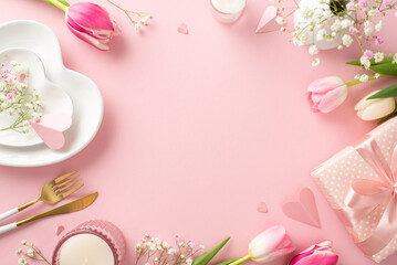 Modern Mother's day table setting. Top view flat lay of plates, cutlery, tulips, gift box, and decorative hearts on pastel pink background with an empty space for advertising or text