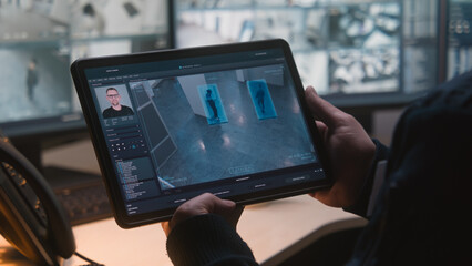 Male security officer controls CCTV cameras in office, uses digital tablet and computers with...