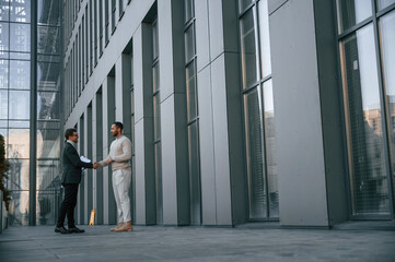 Fototapeta premium With notepat and documents. Businessman in formal clothes is with black man outdoors in the city