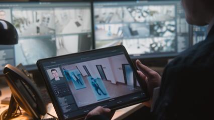 Male security officer controls CCTV cameras in office, uses digital tablet and computers with surveillance camera footage playback on screens. High tech security system. Monitoring and social safety.