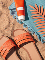 Bright summer beach vacation or travel lifestyle concept flat lay with suncream and a flip flops on the sand. 