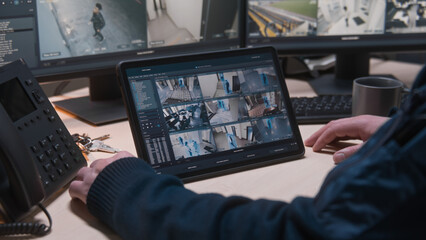 Security operator controls CCTV cameras in office, uses digital tablet and computers with...