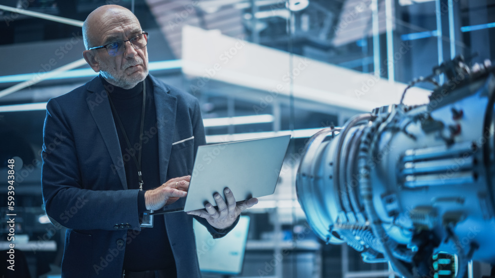 Poster middle aged industrial engineer working on a futuristic jet engine, standing with laptop computer in